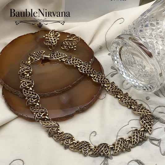 Gold leaf necklace and earrings on a decorative surface with 'BaubleNirvana' branding.