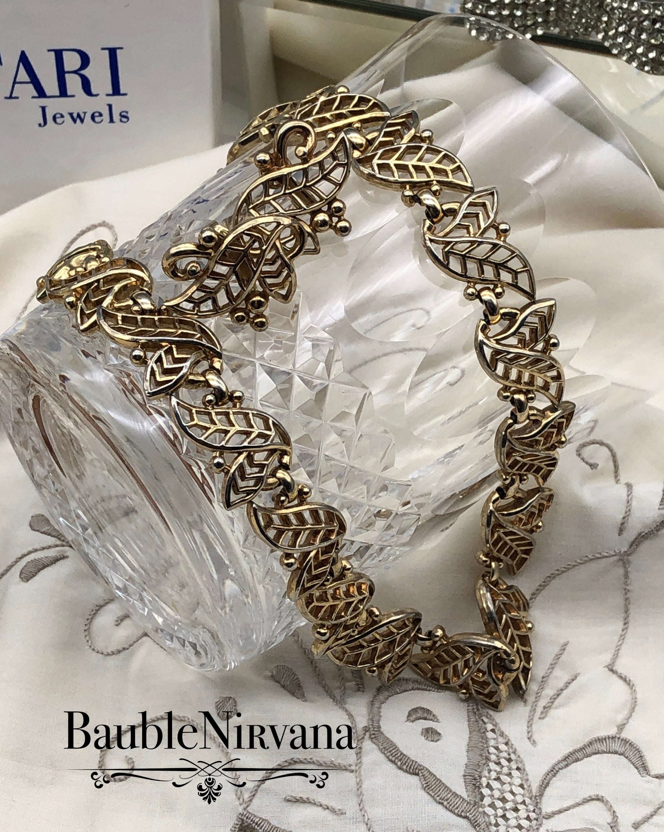 Gold necklace & earrings decorative surface with 'BaubleNirvana' branding.